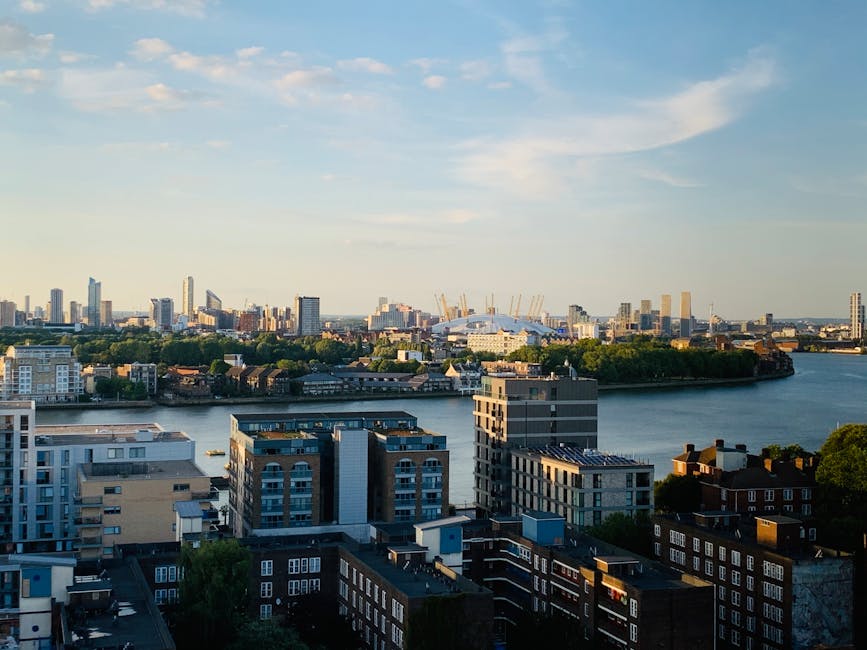 A cityscape featuring a dense cluster of modern high-rise office buildings and residential towers with glass facades reflecting sunlight, set behind a row of low-rise brick houses with pitched roofs and small front gardens. The skyscrapers vary in height, with some structures displaying corporate signage such as HSBC and Citibank. The scene is captured in daylight with clear skies, highlighting the contrast between the contemporary urban skyline and the traditional residential dwellings in the foreground. This image visually emphasizes the juxtaposition of residential areas and commercial development, illustrating potential contexts for private waste handling and alternative rubbish collection services offered by companies like House Clearance Docklands near London City Airport in the Docklands area.